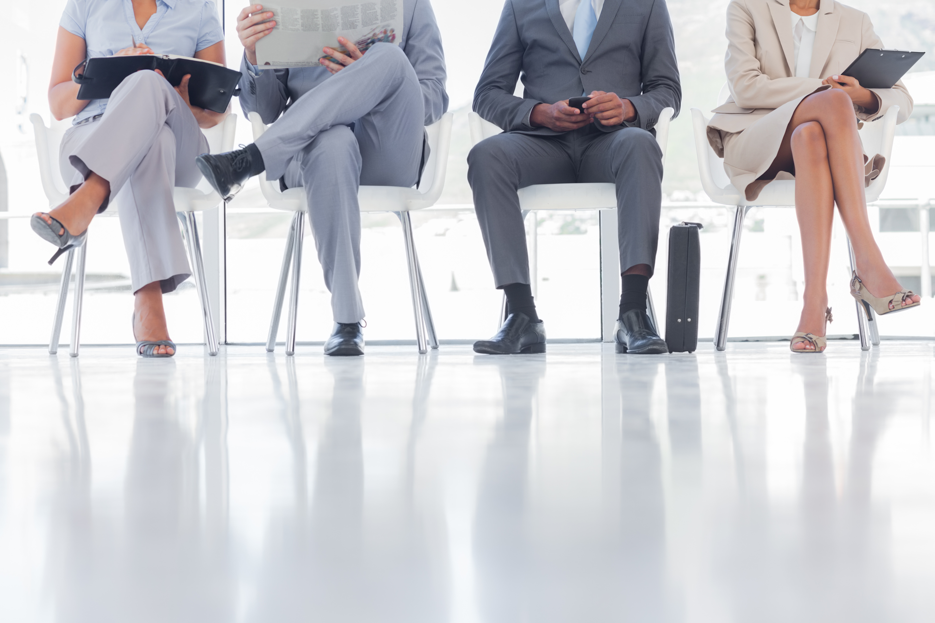 Men and women in professional clothes seated in waiting room reading documents